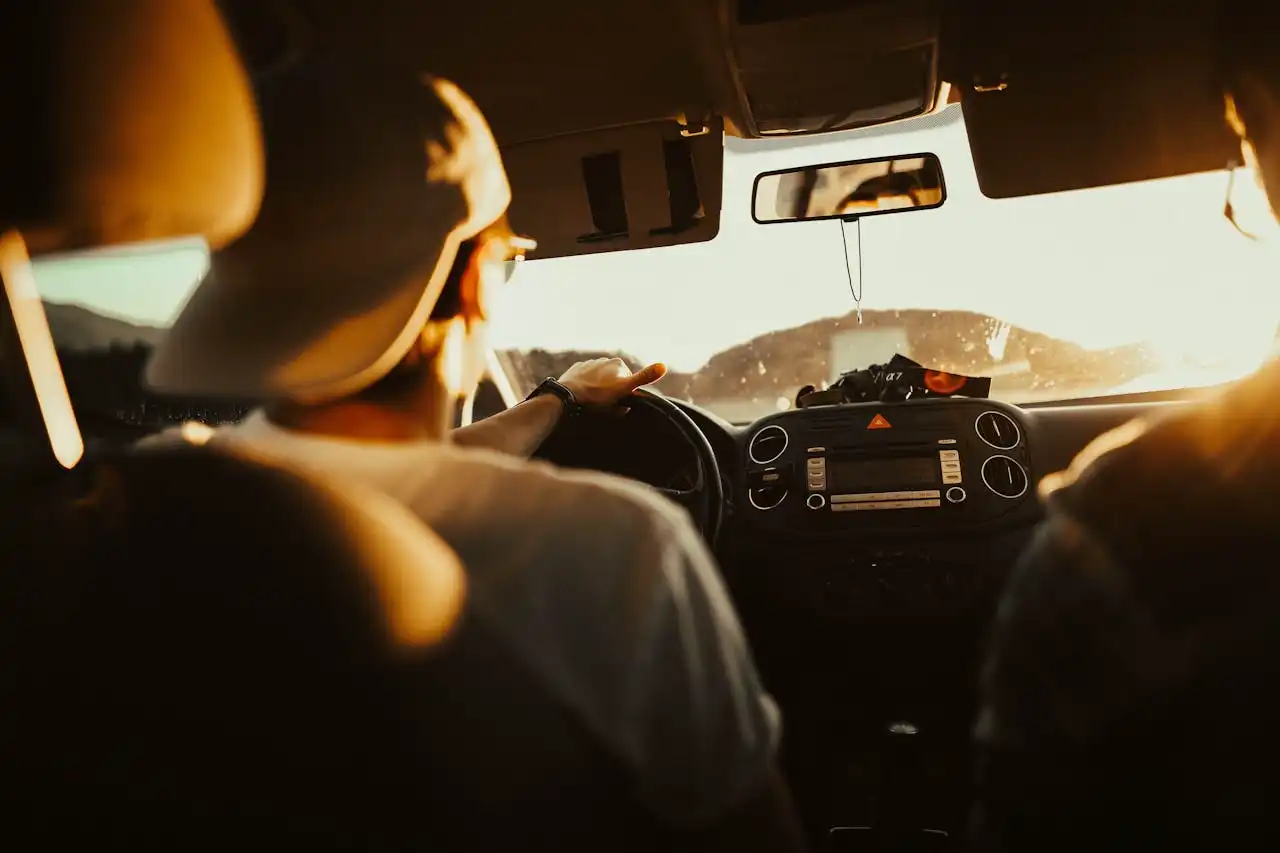 Conducteur en voiture au coucher du soleil, symbolisant un départ vers une nouvelle région.