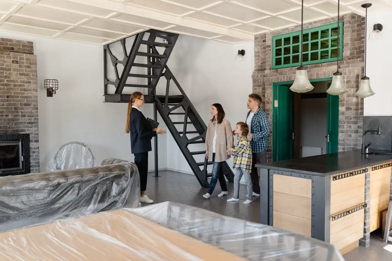 Intérieur d'une maison moderne avec une cheminée en briques, une cuisine équipée, et une famille en visite avec un agent immobilier.